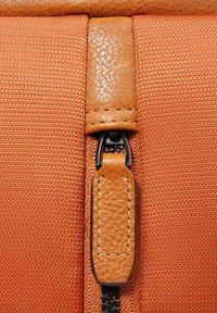 Oranje textiel met een bruine leren accent en ritssluiting. Heeft contrasterende stiksels en metalen hardware detail.