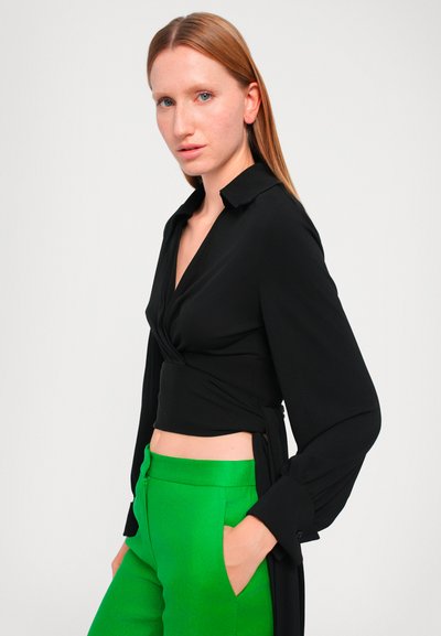 Top noir à manches longues, décolleté en V, avec un détail de n�œud sur le côté, associé à un pantalon taille haute vert fluo avec des poches latérales.