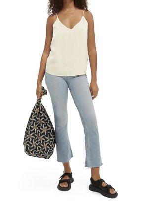 Weißes Satin-Camisole mit V-Ausschnitt, hellblaue, verkürzte Schlagjeans, schwarze gemusterte Tasche und schwarze Sandalen mit Riemchen und dicken Sohlen.