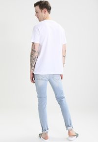 White cotton t-shirt, short sleeves, relaxed fit, paired with light blue denim jeans, slim fit, subtle distressing, worn with slip-on shoes.