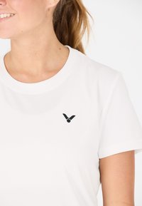 Hvid t-shirt med korte ærmer, lavet af glat stof, med et lille sort logo på venstre brystområde og en rund halsudskæring.
