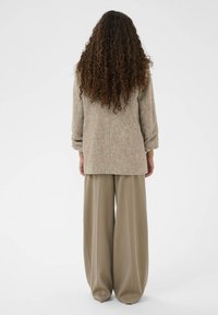 Bežna pletena zunanja oblačila z zavitimi rokavi, v kombinaciji s širokimi, ohlapnimi svetlobrunnimi hlačami. Enostaven dizajn, minimalne podrobnosti.