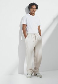 Balts kreklu ar apaļu kaklu, kas kombinēts ar beigu krāsas sporta biksēm ar elastīgu jostu, sānu kabatām un brīvu piegriezumu. Gaišas krāsas sporta apavi.