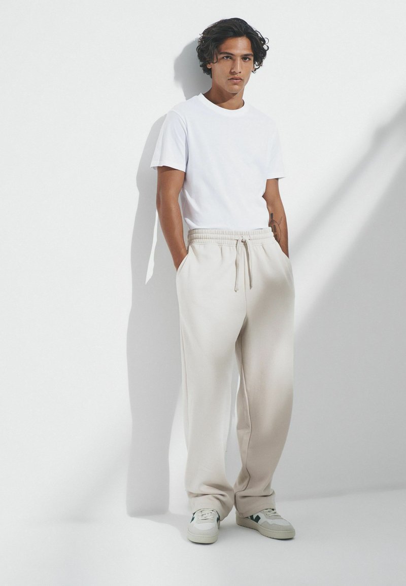 Balts kreklu ar apaļu kaklu, kas kombinēts ar beigu krāsas sporta biksēm ar elastīgu jostu, sānu kabatām un brīvu piegriezumu. Gaišas krāsas sporta apavi.