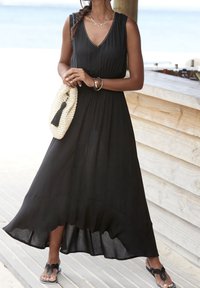 Svart, ärmlös maxiklänning med en utsvängd fåll och V-ringning. Bärs med en vävd handväska med en tofs, i kombination med sandaler.