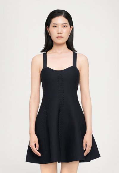 Robe tricotée noire avec un corsage ajusté, des bretelles larges et une jupe évasée. Présente des détails texturés sur les côtés avec un motif symétrique.