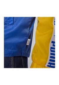 Niebieskie i żółte kurtki w kratkę, z boczną metką na niebieskiej kurtce oraz wyraźnym nadrukiem na żółtej kurtce.