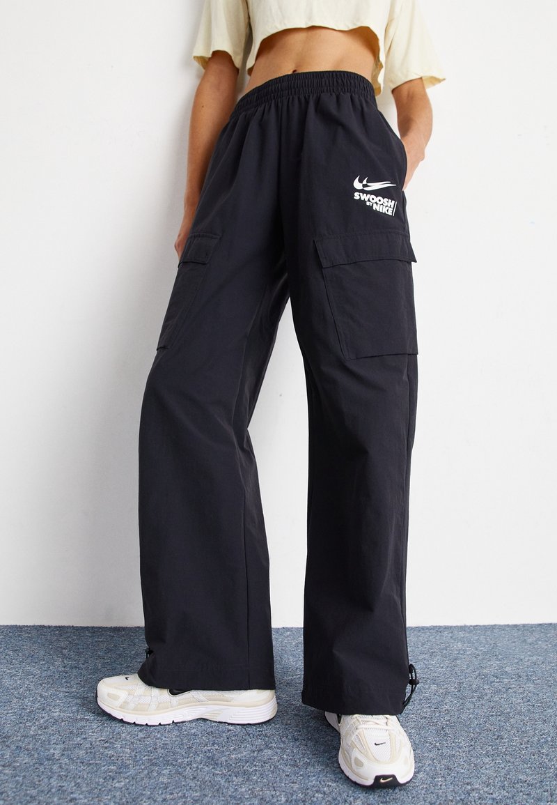 Black cargo pants with a loose fit, featuring an elastic waistband, side pockets, and a white Nike logo on the front. Textured fabric.