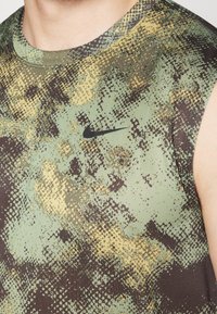 Débardeur de sport en vert, marron et jaune avec un motif texturé pixelisé ; logo Nike noir sur la poitrine.