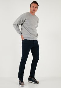 Sivi pulover z okroglim izrezom, v kombinaciji z temno modrimi ožjimi hlačami. Manekenka nosi udobne teniske s temno modro podlago in sivimi detajli.