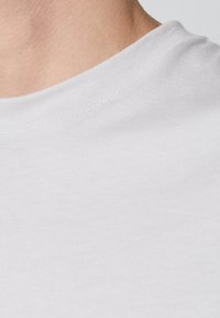 Vit bomull t-shirt med rundad halsringning, slät textur och synliga sömdetaljer vid halsringningen.