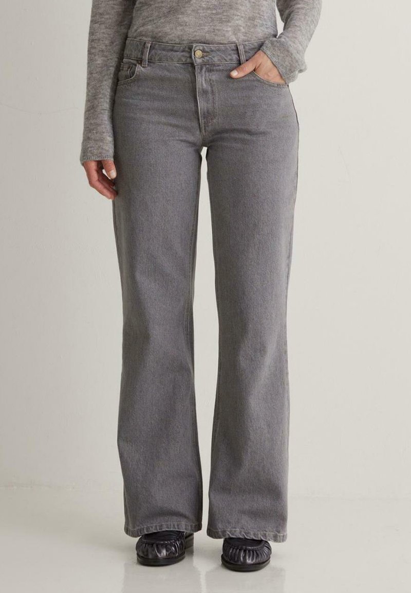 Grijze denim flared jeans, hoog in de taille met een knoopsluiting en zijzakken, gecombineerd met zwarte instapschoenen. Gladde textuur.