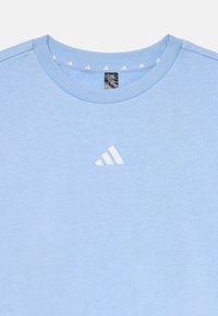 Jasnoniebieska bluza wykonana z miękkiego materiału, z okrągłym dekoltem i małym białym logo Adidas na piersi.