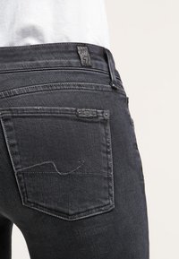 Pantalones vaqueros de mezclilla negra con un diseño clásico, de textura suave, con un bolsillo trasero acentuado por costuras en contraste y una etiqueta de la marca.
