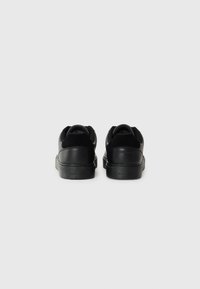 Zwarte sneakers met een gladde leren bovenkant en suède accenten, een dikke zool en merkdetail op de hiel. Achteraanzicht weergegeven.