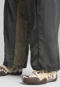 Zwarte en olijfgroene gestreepte broek met een glanzende textuur; gecombineerd met beige camouflage schoenen met een spikey zool en een veilige pasvorm.