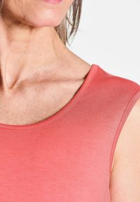 Koraalkleurig mouwloos topje op schouderhoogte, met een gladde textuur en ronde halslijn, met een lichte kleurverloop en minimale stiksels.