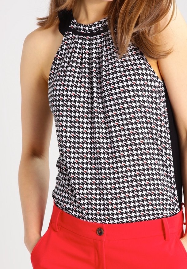 Top de halter de patrón de pata de gallo en blanco y negro con acentos rojos, diseño drapeado y escote negro, combinado con pantalones rojos.