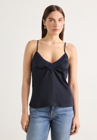 Navy satin cami med tynne justerbare stropper, V-hals og subtile rynker i midten for tekstur og form.