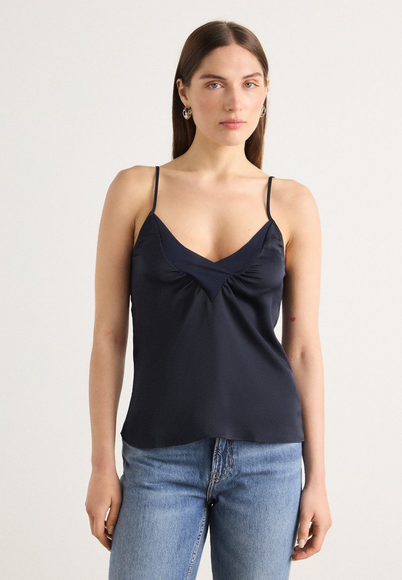 Navy satin cami med tynne justerbare stropper, V-hals og subtile rynker i midten for tekstur og form.