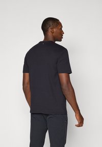 Tricou scurt, negru, cu mânecă scurtă și decolteu rotund, având un logo discret pe spate, realizat dintr-un material neted.