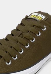Sneaker Converse All Star verde oliva con lacci in tessuto passati attraverso occhielli argentati e suola in gomma bianca con striscia nera.