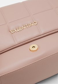 Borsa in pelle rosa morbido di Valentino con un design trapuntato, hardware dorato e un logo prominente. Dettaglio di chiusura circolare sul fronte.