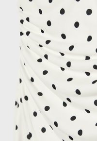 Tissu blanc à pois noirs, avec des détails froncés ou plissés créant des plis doux.