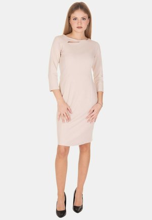 Vestito aderente beige chiaro con maniche a 3/4, caratterizzato da una scollatura rotonda e un'apertura a goccia. Indossato con décolleté nere.