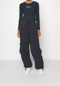 Námořnická dlouhá rukávová košile s bílým logem "Pepe Jeans London", doplněná o volné černé cargo kalhoty a bílé tenisky.