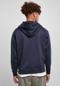 Marineblå hettegenser med ribbet mansjetter og hem, laget av mykt stoff, med en ensfarget design og en avslappet passform.