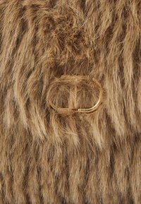 Tessuto in pelliccia sintetica marrone con fibre lunghe. Presenta un accentuato logo ovale tono oro. Aspetto strutturato con una sensazione morbida e peluche.
