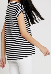 Černobílý pruhovaný tričko s krátkým rukávem a volným střih. Tkanina se zdá být jemná; zakřivený lem a kontrastní detaily límce.