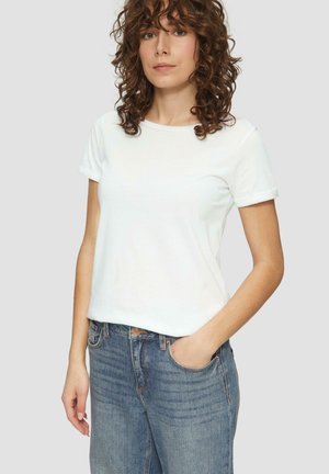 Weißes Baumwoll-T-Shirt mit hochgekrempelten Ärmeln, rundem Ausschnitt und lässiger Passform. Das Model trägt blaue Jeans mit den Händen in den Taschen.