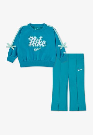 Sweat-shirt Nike bleu sarcelle avec logo blanc et nœuds sur les manches, associé à un pantalon bleu sarcelle assorti avec des logos Nike swoosh blancs.
