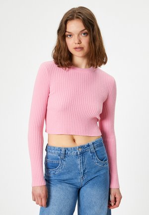 Pull court à manches longues en rose pastel avec texture côtelée. Associé à un jean taille haute bleu clair avec des poches.