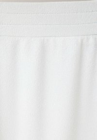 Gros plan sur un tissu blanc texturé avec un détail de ceinture côtelée horizontale en haut.