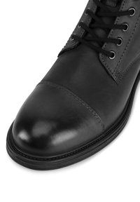 Czarne skórzane botki z zaokrąglonym noskiem, sznurowanym zapięciem i kontrastowym szwem. Gładka tekstura z eleganckim wykończeniem.