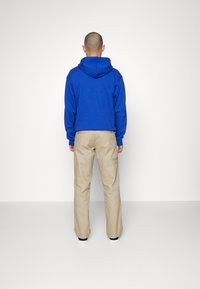 Sudadera azul con capucha y corte relajado, combinada con pantalones rectos beige. Ambos artículos tienen un diseño minimalista y texturas suaves.