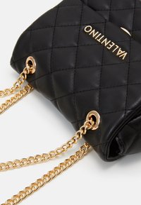 Borsa a tracolla in pelle nera trapuntata con catene e accessori in oro, con il logo "Valentino" in oro sul fronte.
