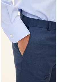 Blaue, strukturierte Hose mit schmaler Passform, seitlichen Taschen und einem glatten Bund. Das hellblaue Hemd verfügt über geknöpfte Manschetten.