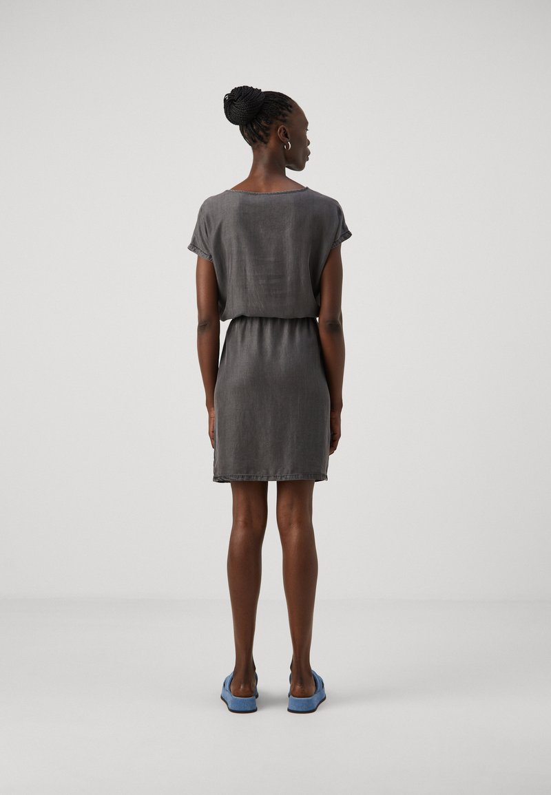 Robe grise à manches courtes, avec une coupe décontractée et une taille froncée. Le tissu a une texture lisse. Associée à des chaussures bleues à enfiler.