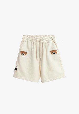 Pantalones cortos de color crema con cintura elástica y cordón, con caras de osito de peluche marrón bordadas sobre cada bolsillo delantero.