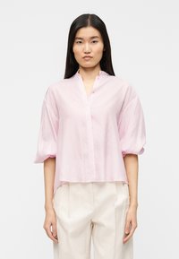 Ροζ ανοιχτόχρωμο πουκάμισο με κοντά μανίκια και γιακά, με ρίγα κουμπιών και ελαφρώς κοντό τελείωμα. Κατασκευασμένο από υφή ύφασμα.