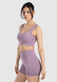 Conjunto atlético morado que consiste en un sujetador deportivo ajustado con tirantes anchos y pantalones cortos de cintura alta, hecho de una tela suave y elástica.