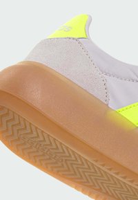 Sneaker features a pinkish upper made of smooth fabric and suede, neon green accents, and a translucent rubber sole with a zigzag tread pattern.