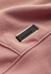 Nahaufnahme von pinkem Stoff mit eingenähten Nähten und einem schwarzen und transparenten rechteckigen Label mit der Aufschrift „ombre“.