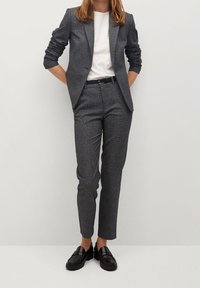 Costume gris à carreaux avec veste sur mesure et pantalon slim, associé à un t-shirt blanc et des mocassins noirs. Texture lisse et design structuré.