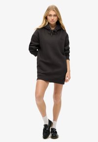 Robe sweat noire avec capuche, manches longues et cordon de serrage. Présente des poignets côtelés, une coupe décontractée et un logo discret sur la poitrine.