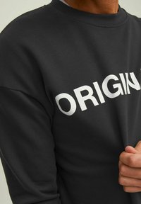 Schwarzer Sweatshirt mit weißem "ORIGIN"-Text auf der Vorderseite. Hergestellt aus weichem Stoff mit Rundhalsausschnitt und gerippten Bündchen.